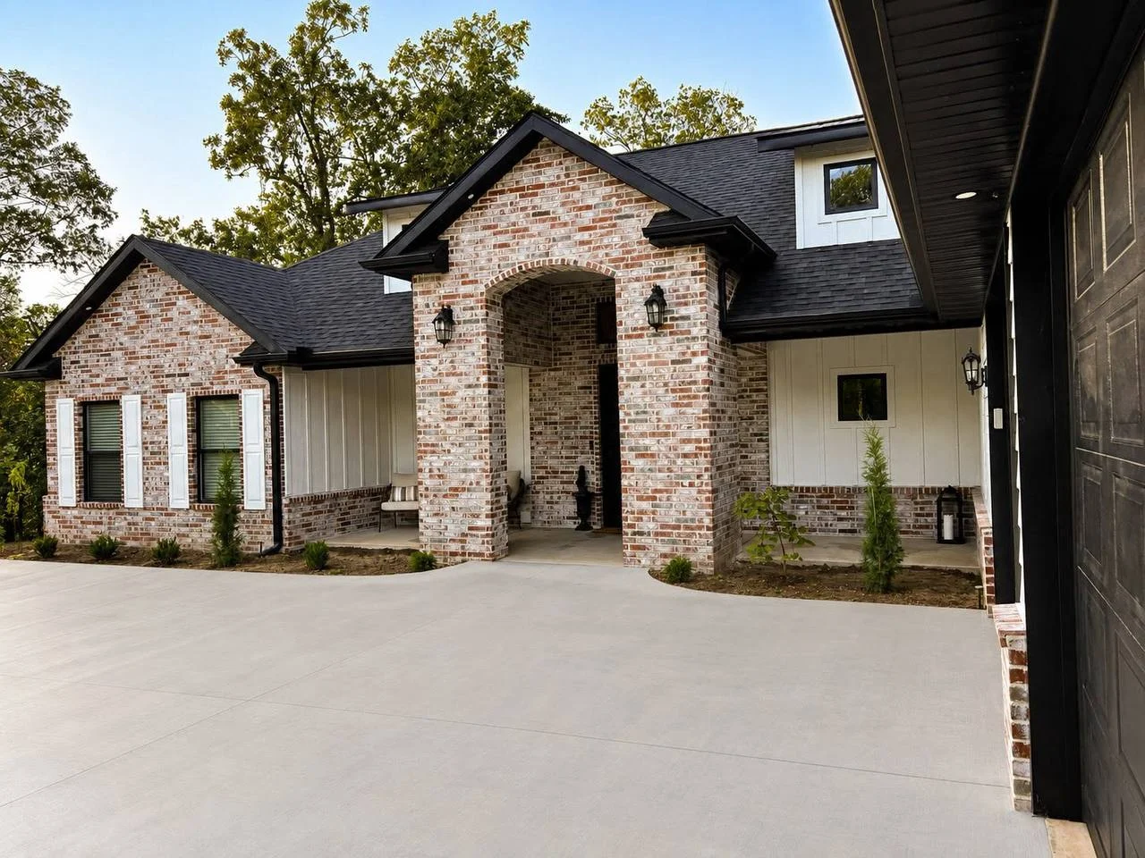 Brick house exterior with arched entryway, black roof, and concrete driveway